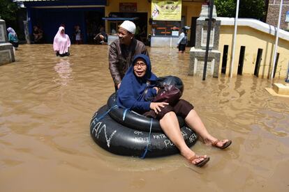 Un hombre empuja a una anciana en flotador hacia un colegio electoral por una calle inundada de Bandung.