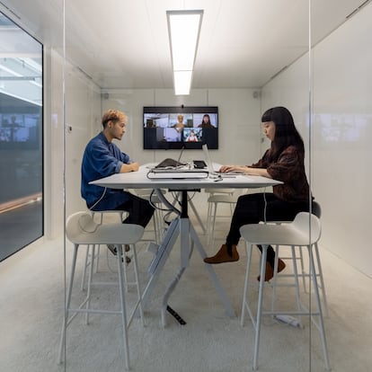 Two businesspeople sitting inside a small cubicle and working on their laptops. Man and woman working in hybrid office cubicle.