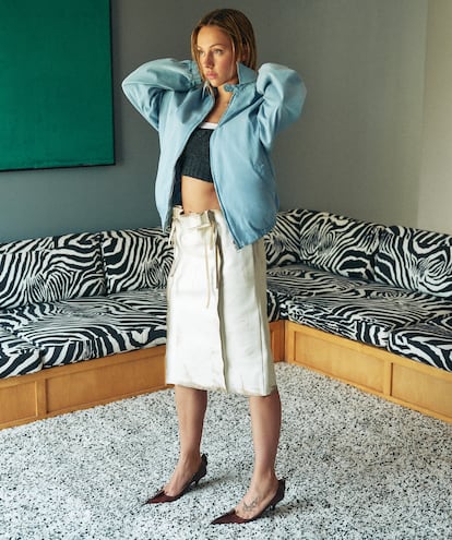 Chaqueta biker azul clara, top corto de punto gris, falda de piel estructurada con
lazos y tacón de piel, todo de PRADA.