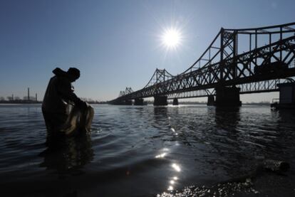 Un trabajador chino recoge basura en el río Yalu, junto al puente que lleva a Corea del Norte.