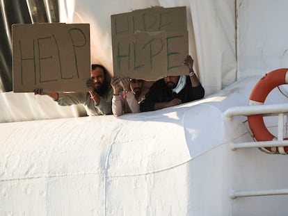 Tres migrantes sujetan carteles en los que piden ayuda, desde un barco con bandera noruega de Médicos Sin Fronteras, frente al puerto de Catania (Italia), este lunes.