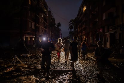 Vecinos y vecinas de Paiporta caminan sobre el lodo y en la oscuridad por el centro de Paiporta, al anochecer del jueves 31 de octubre de 2024.