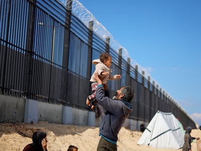 Naser Abu Mustafa, a Palestinian displaced by Israeli attacks, holds his granddaughter in his arms next to the border fence between Gaza and Egypt.