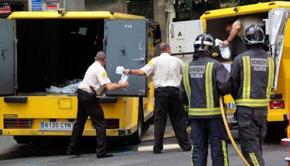 Guardas de seguridad trasladan las sacas de dinero del furgón incendiado a otro vehículo.