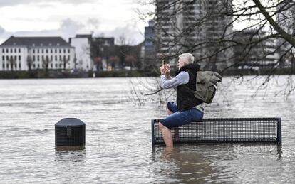 Un hombre hace una foto con su telefono, sentado en un banco en la orilla inundada del río Rin en Colonia, Alemania. La marea alta causada por la lluvia y el deshielo amenaza la navegación comercial en el mayor río de Alemania, el Rin. 