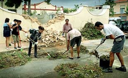 Vecinos de Alginet, ayer, recogiendo los escombros de la pared que un rbol derrib durante la tormenta del mircoles.