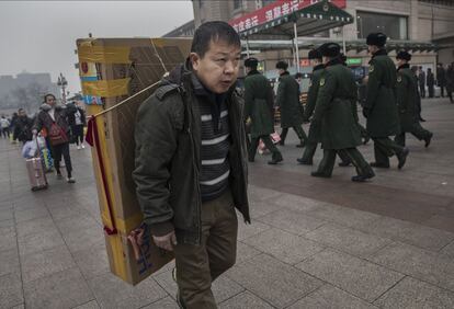 Un hombre chino transporta una televisión en su espalda mientras se dirige a la estación de tren de Pekín.