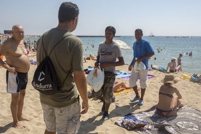 Un agent, d'esquena, demana el material a dos venedors a la platja de la Nova Icria.