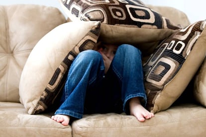 Un niño se esconde entre los cojines del sofá.