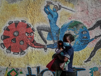 Una mujer con un bebé en brazos pasa delante de un mural que simboliza la lucha contra el coronavirus en una calle de Kericho, Kenia.