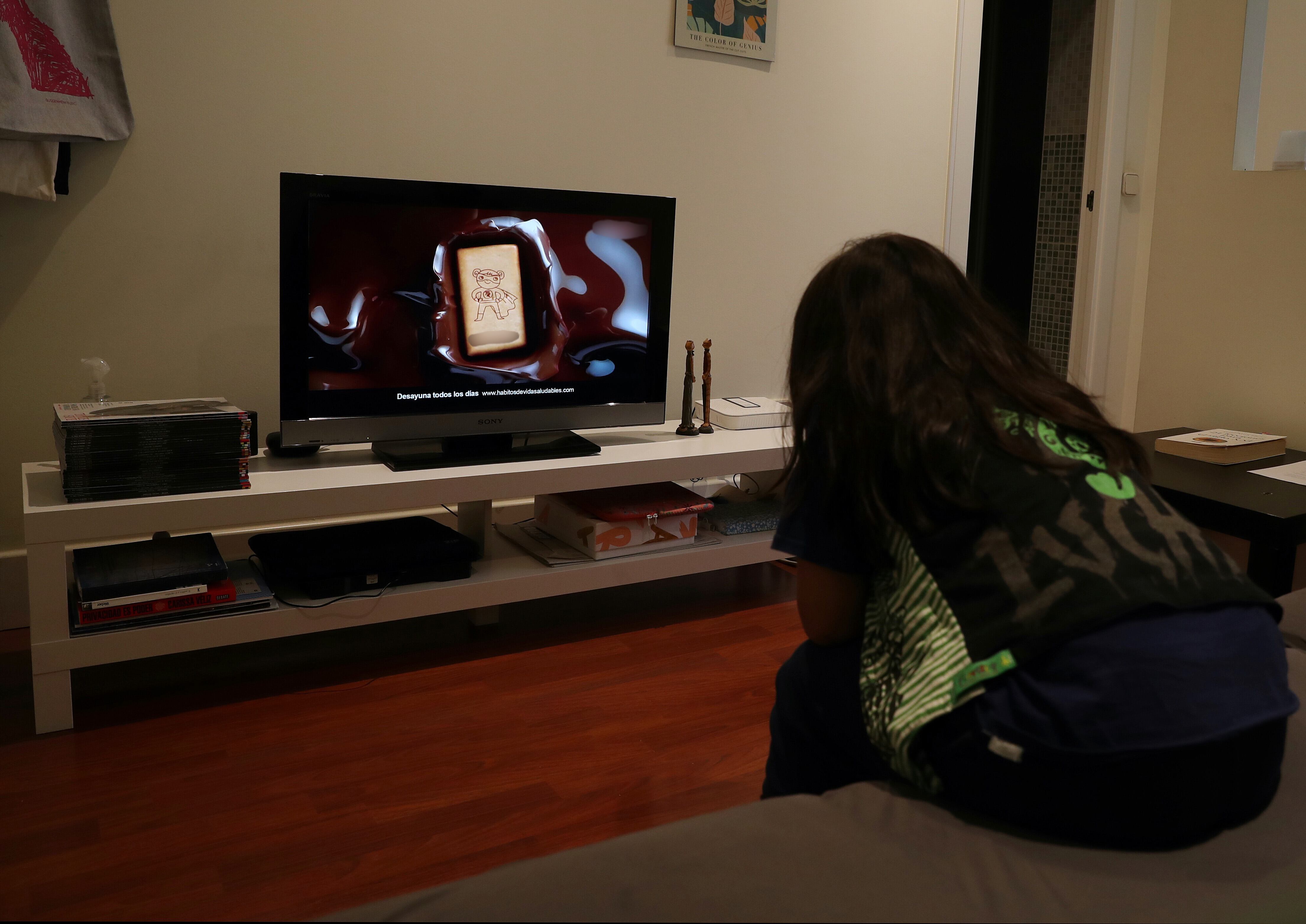 Un niño ve en la television en su casa publicidad de alimentos poco saludables. 