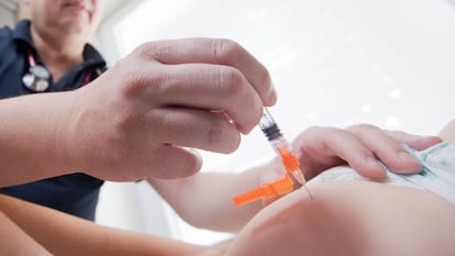 Un trabajador sanitario administra una dosis de la vacuna triple vírica a un niño.