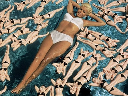 Jayne Mansfield flota en una piscina de California en 1957. Eso que la rodean no son muñecas de sí misma, no, es todavía mejor: son botellas con su forma.