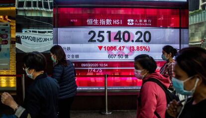 Un grupo de personas camina frente a un panel electrónico que muestra la evolución del Hang Seng de Hong Kong este lunes. Este índice cayó un 4,23% en la sesión, en línea con las bajadas de las Bolsas asiáticas.