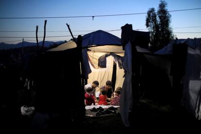 Dos hombres migrantes y cuatro bebés se sientan dentro de una carpa en un campamento improvisado en la isla de Lesbos (Grecia).