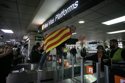 Un manifestante se enfrenta al personal de seguridad al saltar sobre un torno de la Renfe para acceder a las vías.