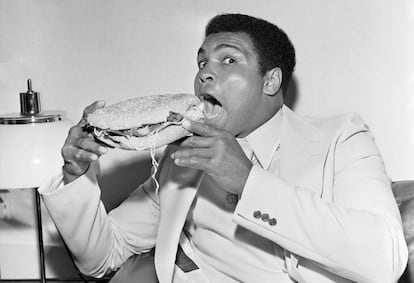 Muhammad Ali a punto de hincar el diente a un bocadillo con lechuga, cebolla y tomate típico del sur de Estados Unidos en 1977.