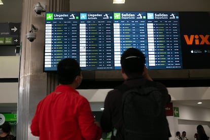 Dos viajeros revisan la información de despegues y llegadas en uno de las pantallas del AICM.