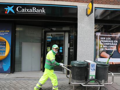 Un operario de limpieza pasa por delante de una oficina de CaixaBank, en Madrid, el 22 de abril.