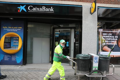 Un operario de limpieza pasa por delante de una oficina de CaixaBank, en Madrid, el 22 de abril.