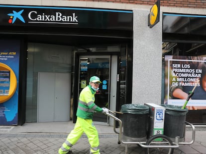 Un operario de limpieza pasa por delante de una oficina de CaixaBank, en Madrid, el 22 de abril.