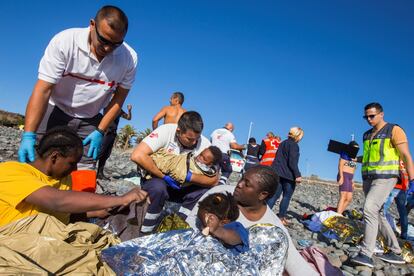 Veinticuatro personas, entre ellas tres bebés y tres menores más, han llegado este viernes en patera a la playa del Águila, en Gran Canaria, 13 de los cuales han sido derivados a centros sanitarios al presentar deshidratación, mareos y cuadros de vómitos tras cinco días en el mar. En la imagen, los miembros del servicio de rescate atienden a los migrantes poco después de su desembarco.