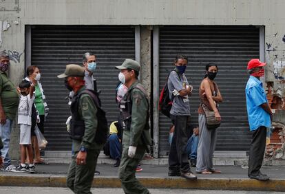 Personas con mascarillas observan a unos agentes de la policía en Caracas, Venezuela.