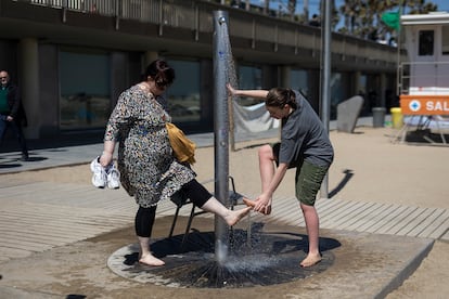 Dos turistas se limpian los pies con agua en la playa de a Barceloneta el pasado miercoles.