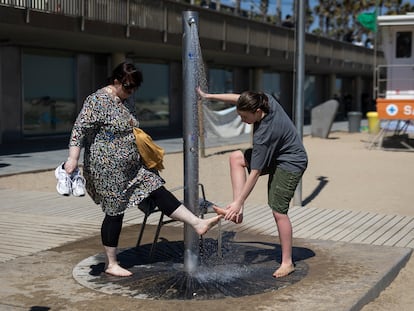 Dos personas se lavan los pies en una ducha de la playa de la Barceloneta.