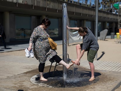 Dos turistas se limpian los pies con agua en la playa de a Barceloneta el pasado miercoles.