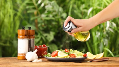 Una mano con una aceitera en espray aliñando una ensalada.