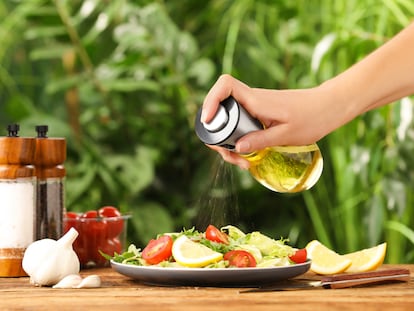 Una mano con una aceitera en espray aliñando una ensalada.