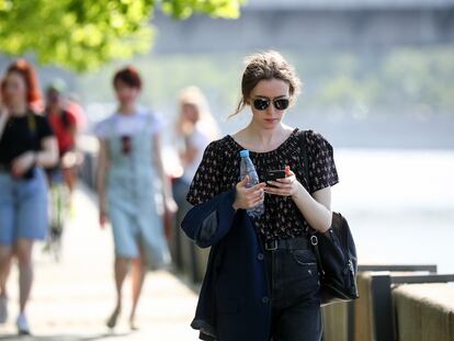 Mulher consulta telefone celular enquanto passeia em Moscou.