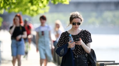 Mulher consulta telefone celular enquanto passeia em Moscou.