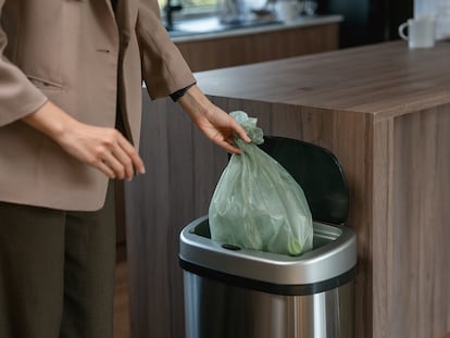 Una persona tirando una bolsa en un cubo de basura en su casa.