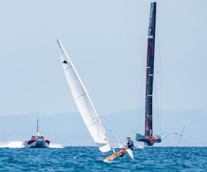 Un patín navega en el mar frente a Barcelona delante de una lancha y de uno de los barcos de la Copa del América.