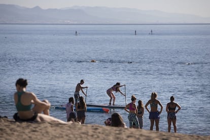 Varias personas hacen deporte en el agua y en la arena de la playa de la Barceloneta.