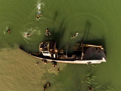 Esta vista aérea muestra a niños nadando junto a los restos de una embarcación en el canal Shatt al-Arab, formado en la confluencia de los ríos Éufrates y Tigris, en la ciudad de Basora, en el sur de Irak. 
