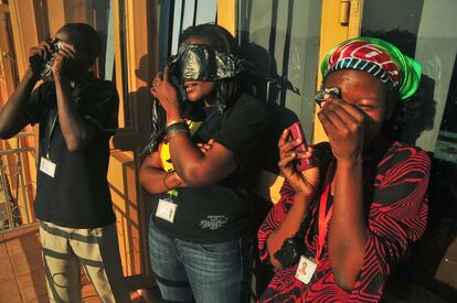 Tres j&oacute;venes ugandeses observan el eclipse a trav&eacute;s de trozos de pl&aacute;stico negro en Kampala. 