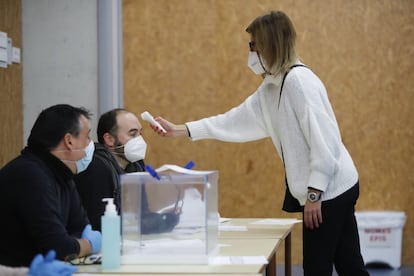 Una trabajadora comprueba la temperatura de los miembros de una mesa electoral en el colegio Mediterrànea, en Barcelona. Para que las elecciones catalanas transcurran con normalidad se ha convocado a formar parte de las mesas electorales a 82.251 personas, entre titulares y suplentes. 31.000 de ellas han presentado alegaciones.