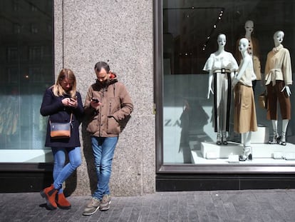 Dos jóvenes usan sus móviles ante una tienda Zara en Madrid.
