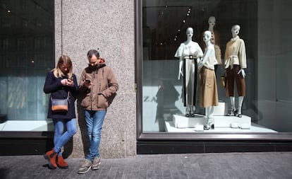 Dos jóvenes usan sus móviles ante una tienda Zara en Madrid.