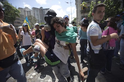 Un manifestante lleva a una mujer abrumada por el gas lacrimógeno disparado por la Policía Nacional Bolivariana en Caracas, Venezuela, el sábado 8 de abril de 2017