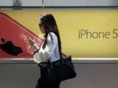 Una mujer utiliza un smartphone mientras camina junto a una publicidad de iPhone 5.