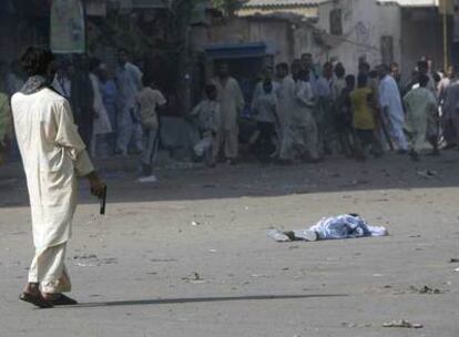 La gente huye de un hombre armado con pistola cerca del cadáver de un chico asesinado en los enfrentamientos de ayer en Karachi.