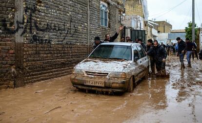 Varios hombres empujan un vehículo atrapado por las inundaciones, en Shiraz (Irán).
