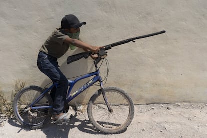 Un niño juega con su arma de madera montado en una bicicleta al término de la marcha.