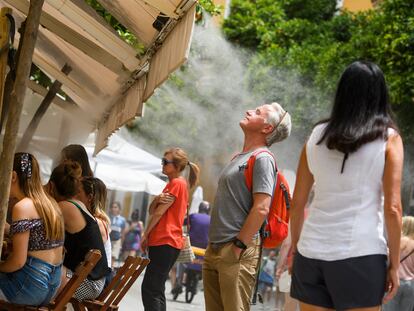 Unos turistas se refrescan con los vaporizadores de un bar en el centro de Sevilla, el viernes.