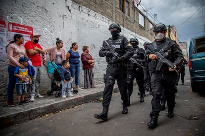 Familias miran a policías armados con máscaras que luchan contra el narcotráfico en la ciudad.