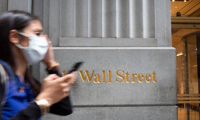 Una mujer con mascarilla pasa frente al edificio de Wall Street en Nueva York.